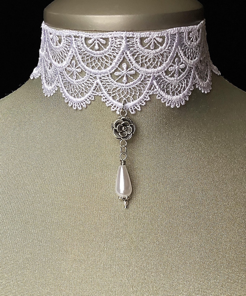May include: White lace choker necklace with a silver flower charm and a pearl pendant.