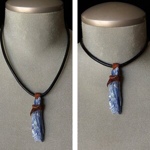 Puede incluir: Un collar de cuero negro con un colgante de cristal de cianita azul. El cristal está envuelto con cordón de cuero marrón.