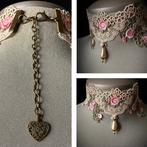 Puede incluir: Un collar gargantilla de encaje delicado con bordados florales de color rosa y verde. El collar presenta un colgante en forma de coraz&oacute;n en una cadena y un colgante de gota de perla.