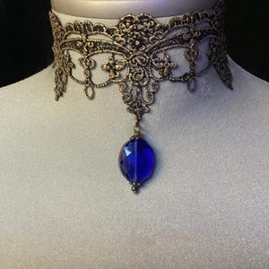 Pode incluir: Um colar de choker de renda dourada com um pingente de pedra preciosa azul.