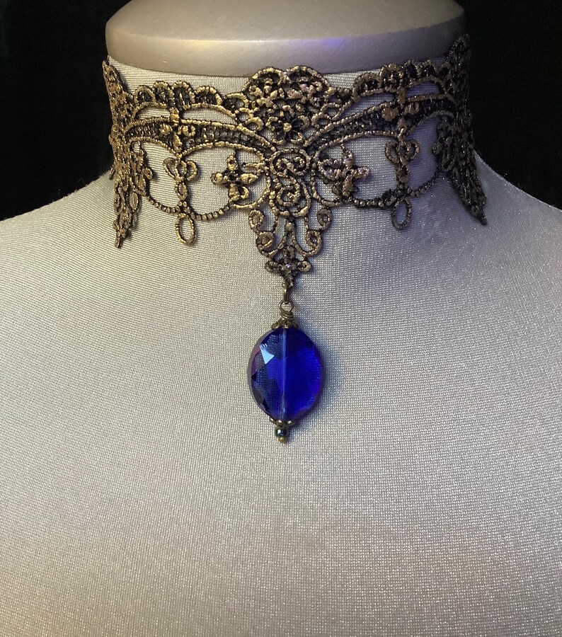 Pode incluir: Um colar de choker de renda dourada com um pingente de pedra preciosa azul.