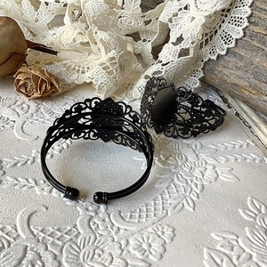 May include: Two black metal bracelets with intricate filigree designs. One bracelet has a round, black cabochon in the center.