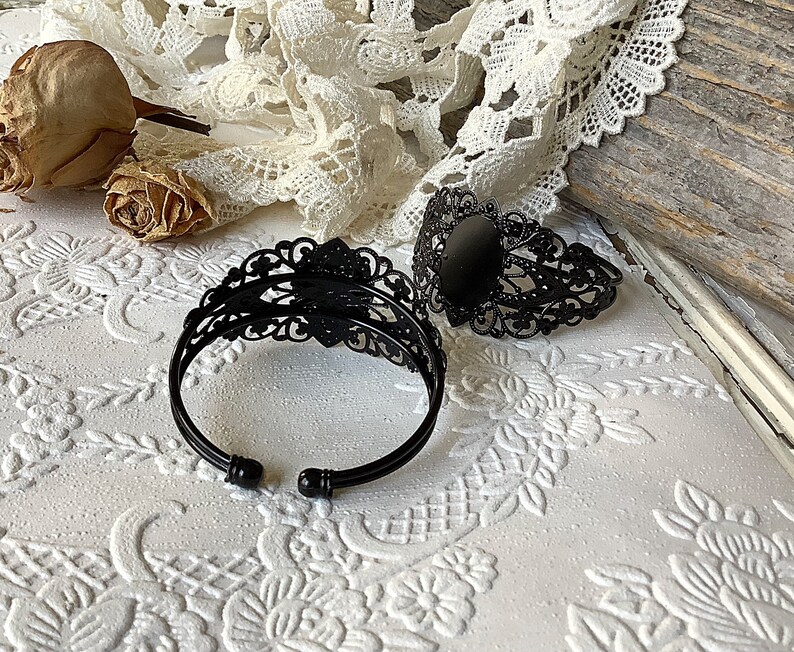 May include: Two black metal bracelets with intricate filigree designs. One bracelet has a round, black cabochon in the center.