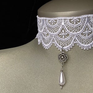 May include: White lace choker necklace with a silver flower pendant and a pearl drop.