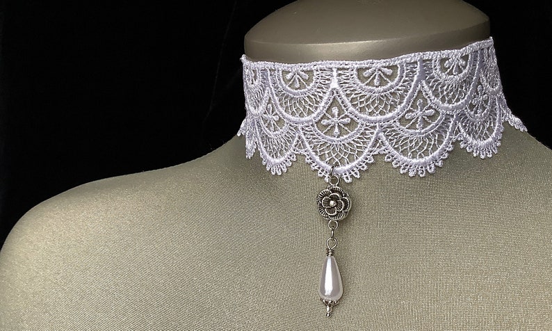 May include: White lace choker necklace with a silver flower pendant and a pearl drop.