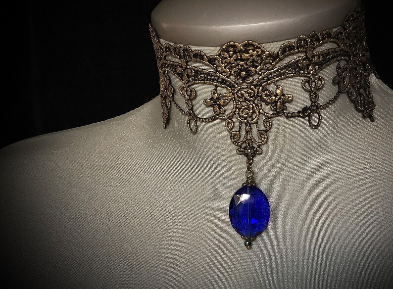 Pode incluir: Um colar de renda dourado com um pingente de pedra preciosa azul.