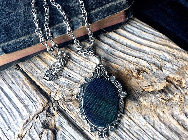 May include: A silver chain necklace with a heart charm and a pendant featuring a dark green and black patterned fabric inside a silver ornate frame.