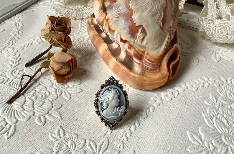 May include: A silver ring with a blue and white cameo of a woman's profile. The cameo is set in a silver oval frame with ornate details.