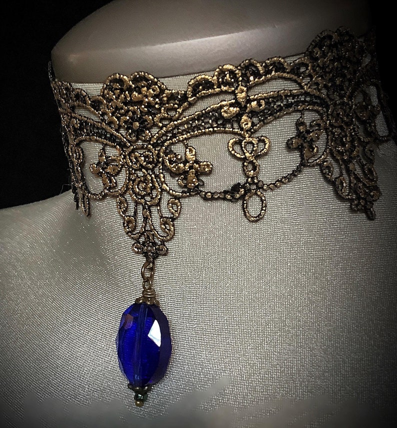 Pode incluir: Um colar de renda dourado com um pingente de pedra preciosa azul.