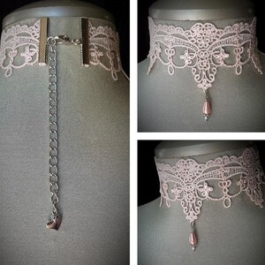 Puede incluir: Un delicado collar gargantilla de encaje rosa p&aacute;lido con una cadena plateada y un colgante de coraz&oacute;n. El encaje presenta un intrincado dise&ntilde;o floral. El collar se muestra en un maniqu&iacute;.