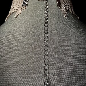 May include: A delicate white lace choker with a silver chain and a heart-shaped pendant. The pendant has a small rose design.