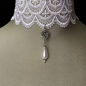 May include: White lace choker necklace with a silver flower charm and a pearl pendant.