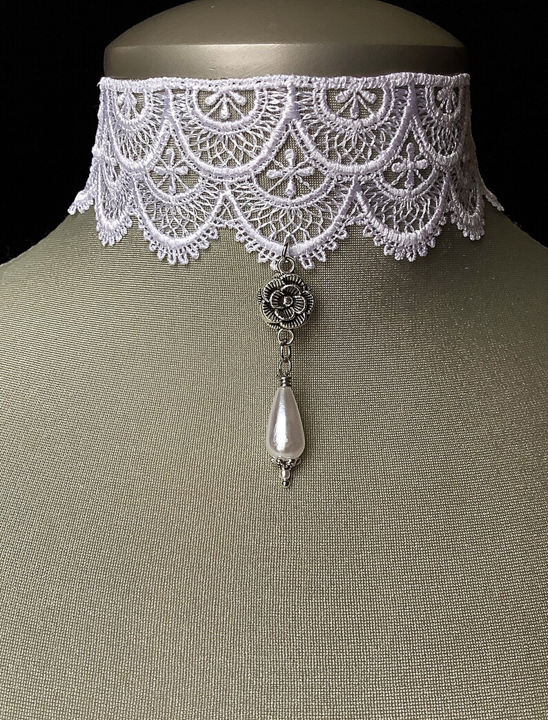May include: White lace choker necklace with a silver flower charm and a pearl pendant.