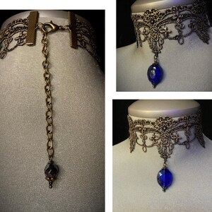 Pode incluir: Um colar de renda dourado com um pingente de cristal azul. O colar tem um extensor de corrente com uma conta de cristal escura.