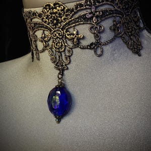 Pode incluir: Um colar de choker de renda dourada com um pingente de pedra preciosa azul.