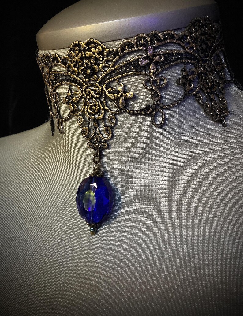 Pode incluir: Um colar de choker de renda dourada com um pingente de pedra preciosa azul.