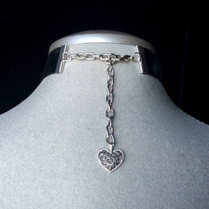 May include: Black velvet choker with a silver chain and a silver heart pendant. The heart pendant has a filigree design.