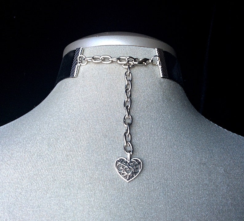 May include: Black velvet choker with a silver chain and a silver heart pendant. The heart pendant has a filigree design.