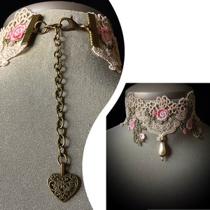 Puede incluir: Un delicado collar gargantilla de encaje con bordados florales de color rosa y verde. El collar presenta un colgante en forma de coraz&oacute;n y una gota de perla.