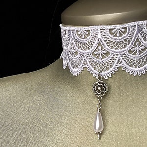 May include: White lace choker necklace with a silver flower pendant and a pearl drop.