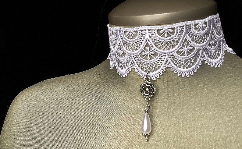 May include: White lace choker necklace with a silver flower pendant and a pearl drop.