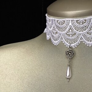 May include: White lace choker necklace with a silver flower charm and a white pearl pendant.