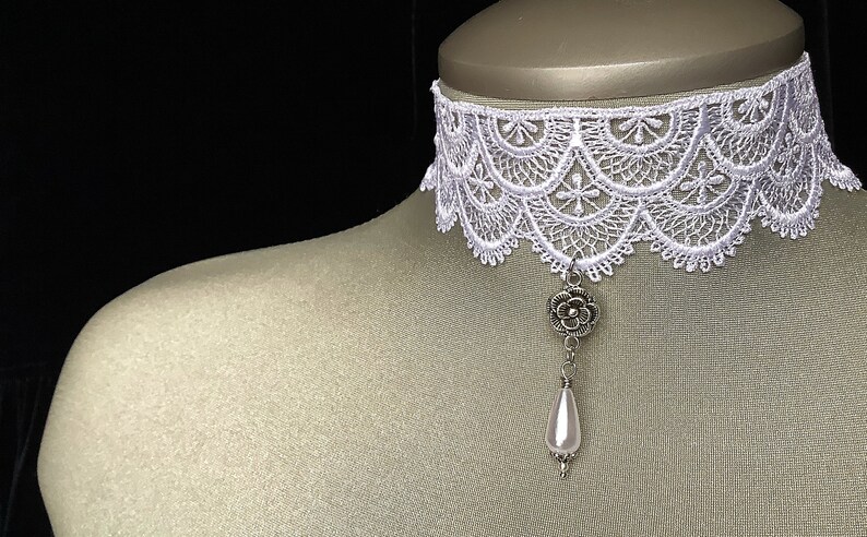 May include: White lace choker necklace with a silver flower charm and a white pearl pendant.