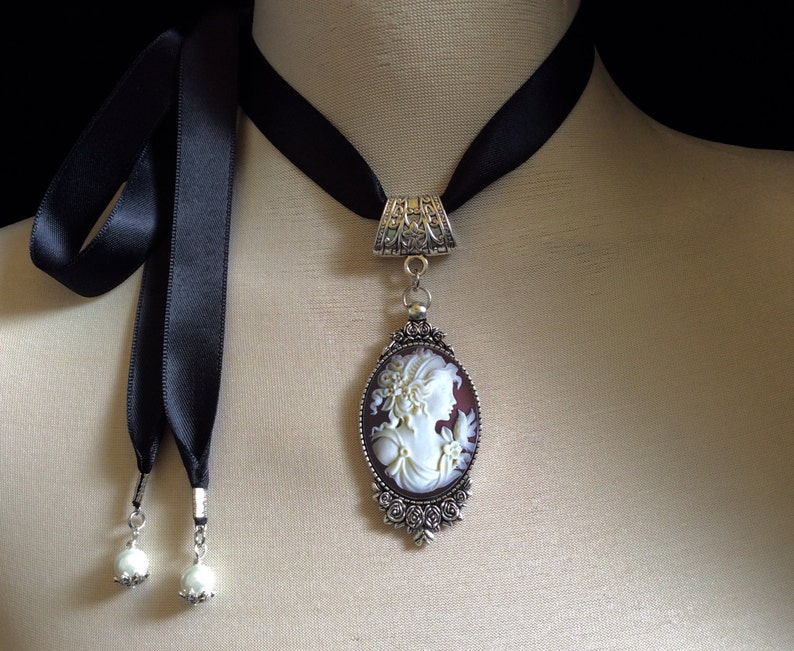 Beautiful, detailed, light ivory and dark wine cameo set in an oval, antique silver pendant with tiny baroque roses and attached to a high quality double sided satin ribbon...round, light ivory pearls are attached to each end of the 25" ties....