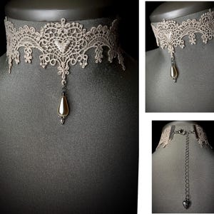 May include: A delicate beige lace choker necklace with a pearlescent teardrop pendant. The necklace has a silver chain closure.