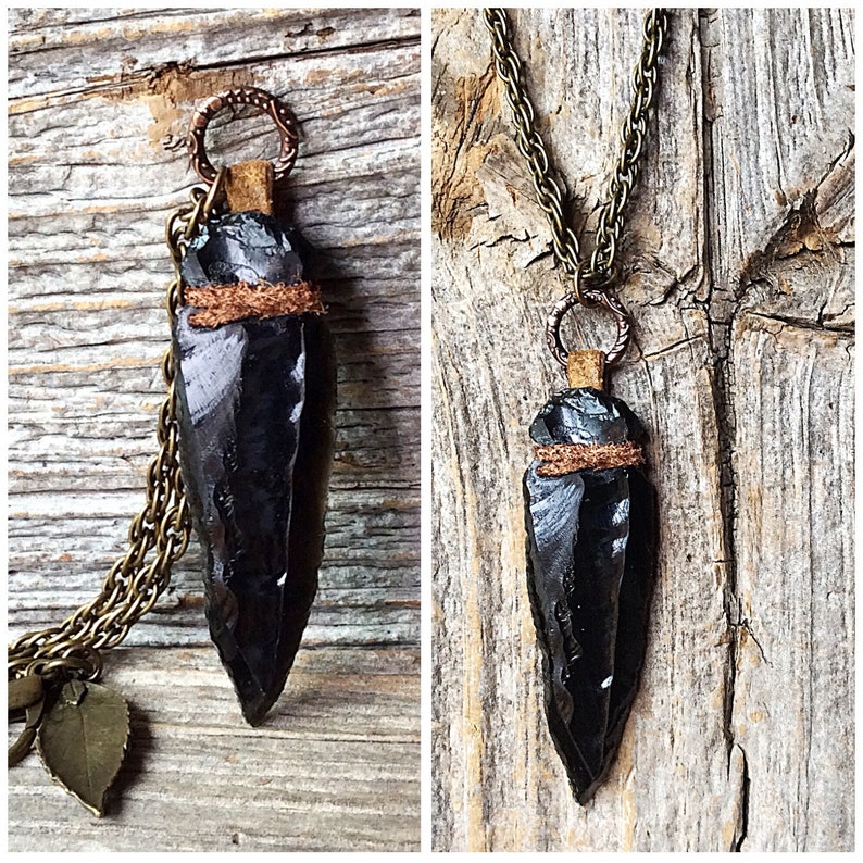 Puede incluir: Un collar con un colgante de punta de flecha de obsidiana negra, con una envoltura de cuero marr&oacute;n y detalles en cobre. El collar est&aacute; en una cadena con un dije de hoja.