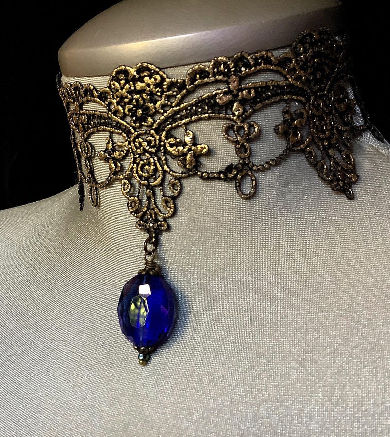 Pode incluir: Um colar de choker de renda dourada com um pingente de pedra preciosa azul.