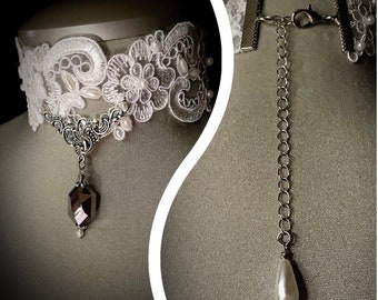 May include: A white lace choker necklace with a silver pendant featuring a faceted black crystal and a pearl drop. The choker has a silver chain extender with a pearl drop.