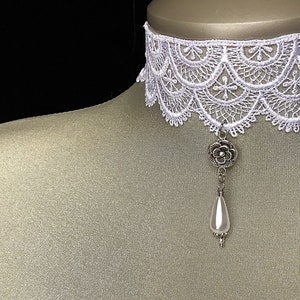 May include: White lace choker necklace with a silver flower pendant and a white pearl drop.