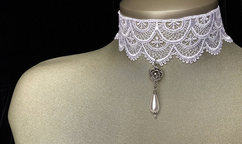 May include: White lace choker necklace with a silver flower pendant and a white pearl drop.