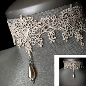 May include: A delicate ivory lace choker necklace with a single pearl pendant. The choker is made of intricate lacework and has a delicate, feminine look.