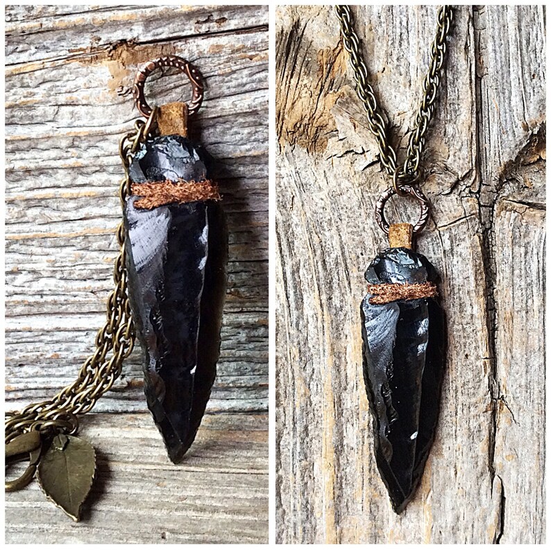 Puede incluir: Un collar con un colgante de punta de flecha de obsidiana negra, con una envoltura de cuero marr&oacute;n y una cadena de lat&oacute;n.