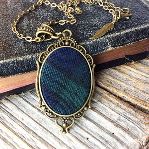 May include: A gold-toned necklace with a dark blue and green plaid fabric pendant in an oval frame.
