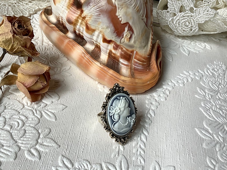 May include: A silver ring with a blue cameo featuring a woman's profile. The cameo is set in a detailed silver frame.
