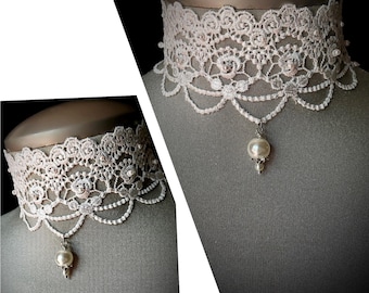 Könnte beinhalten: Ein zarter, cremefarbener Spitzen-Choker mit gewelltem Rand und einem hängenden Perlenanhänger. Das filigrane Spitzendesign weist florale und perlenbesetzte Akzente auf und schafft ein elegantes und romantisches Accessoire. Die Halskette wird auf einer Schaufensterpuppe präsentiert.