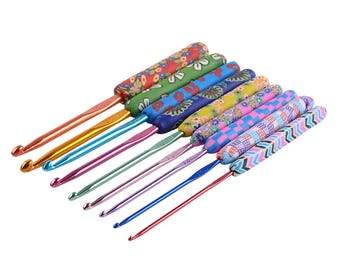May include: A set of crochet hooks with patterned handles in various colours. The metal hooks are in shades of gold, pink, and blue. The handles display floral, geometric, and abstract patterns, offering a range of design choices.