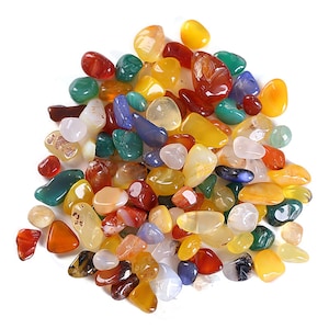 May include: A collection of polished gemstones in various colors, including red, green, yellow, and blue. The stones are smooth and rounded, with a natural, organic appearance. The gemstones are of different sizes and shapes, and are scattered across a white surface.