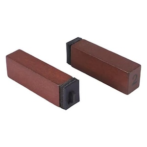 May include: Two rectangular wooden furniture risers with a dark brown finish. Each riser has a black rubber base and a number "2" printed on one end. The risers are designed to elevate furniture.