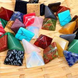 May include: A collection of small, polished stone pyramids in various colours and patterns, including blue turquoise with black veining, red jasper, green unakite, black snowflake obsidian, translucent opalite, and speckled beige stone.