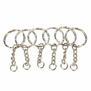 May include: Six silver keyrings with split rings and short chain links. Each keyring has a small, round ring at the end of the chain. The keyrings are arranged in a row against a white background.