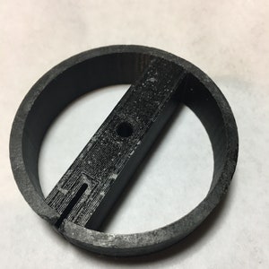 May include: A black plastic ring with a flat, rectangular bar across the center. The bar has a small hole in the center and a slot cut into it.
