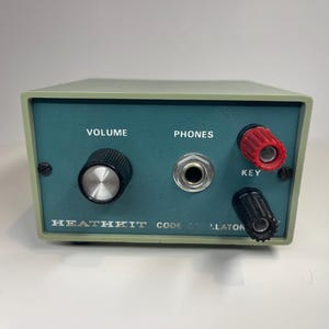 May include: A vintage Heathkit code oscillator in a light green metal housing with a teal front panel. It features a black volume knob, a central headphone jack, and two binding posts labeled KEY, one red and one black, with white text.