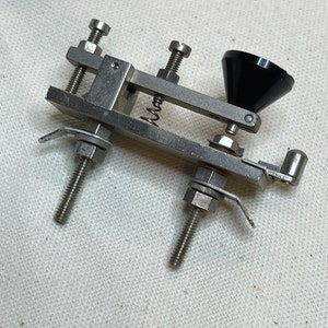 May include: A silver metal clamp with a black plastic cone on the end. The clamp has two adjustable screws and a spring.