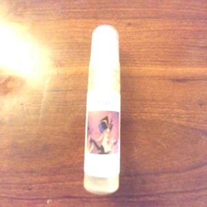 May include: A small, clear glass bottle with a white label featuring a colorful illustration of a butterfly. The bottle is on a wooden surface.