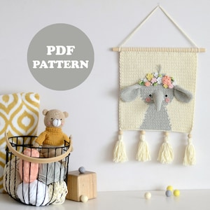 Peut inclure: Une tapisserie murale en crochet représentant un éléphant avec une couronne de fleurs, des glands crème et le texte "PDF PATTERN".