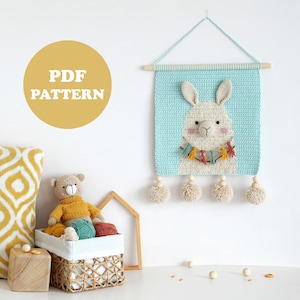May include: A crochet wall hanging featuring a llama with a colorful tassel garland. The hanging is light blue with a white llama face and has wooden beads and pom-poms. The text "PDF PATTERN" is on a yellow circle.
